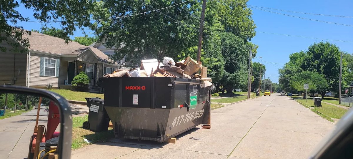 Black roll-off dumpster loaded with debris on a residential street.