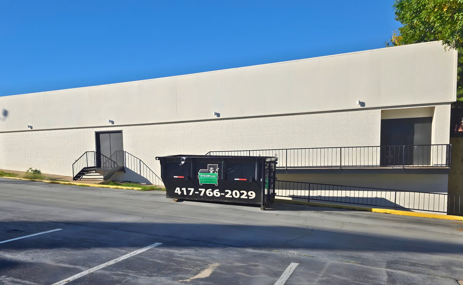 Black roll-off dumpster staged in a paved parking lot.
