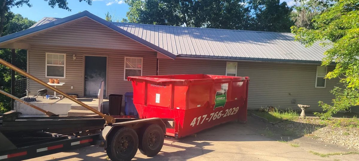 Red roll-off dumpster and trailer in front of a house with a new metal roof
