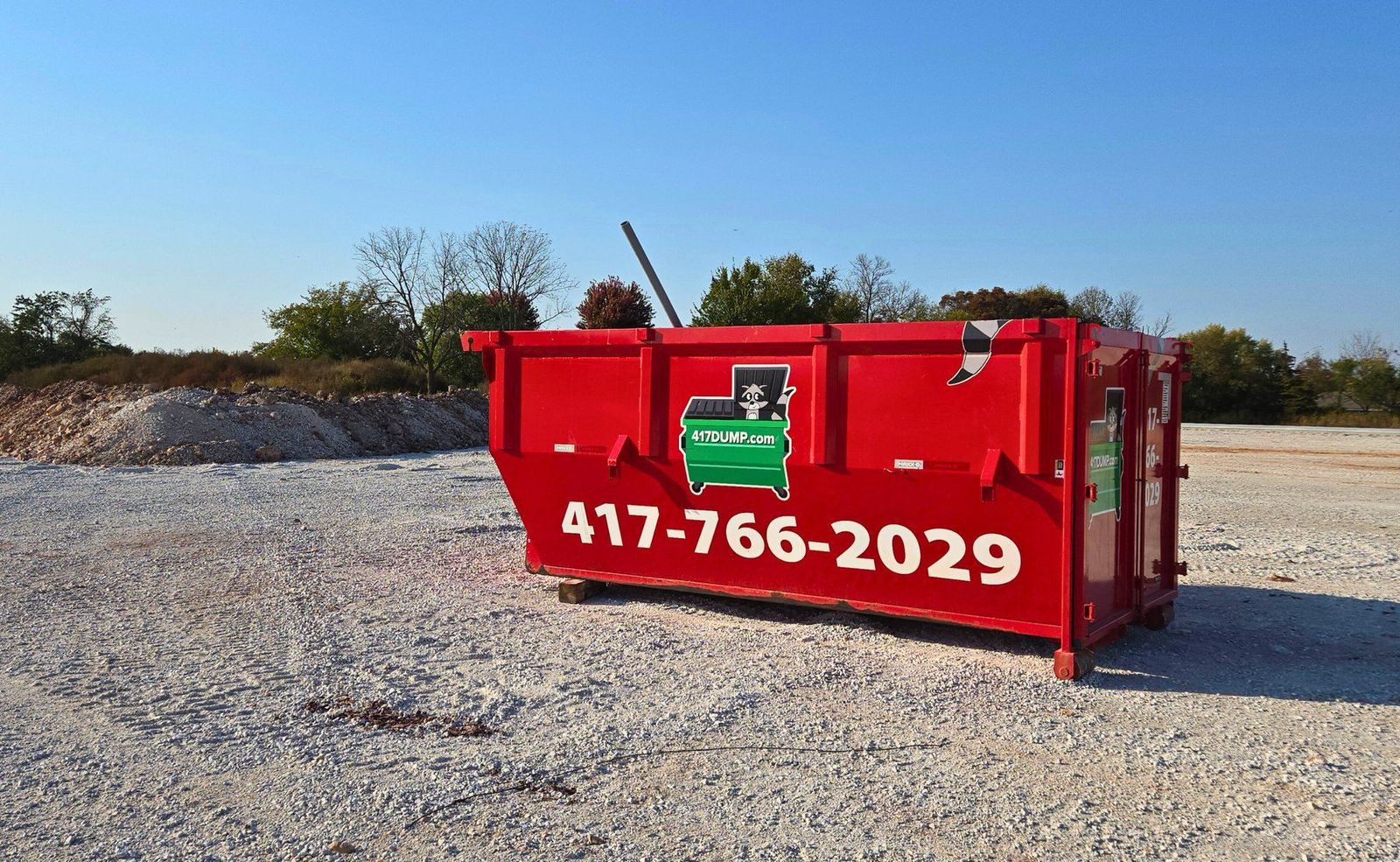 Red 417 Dumpster Rental roll-off dumpster on a gravel pad in golden-hour light
