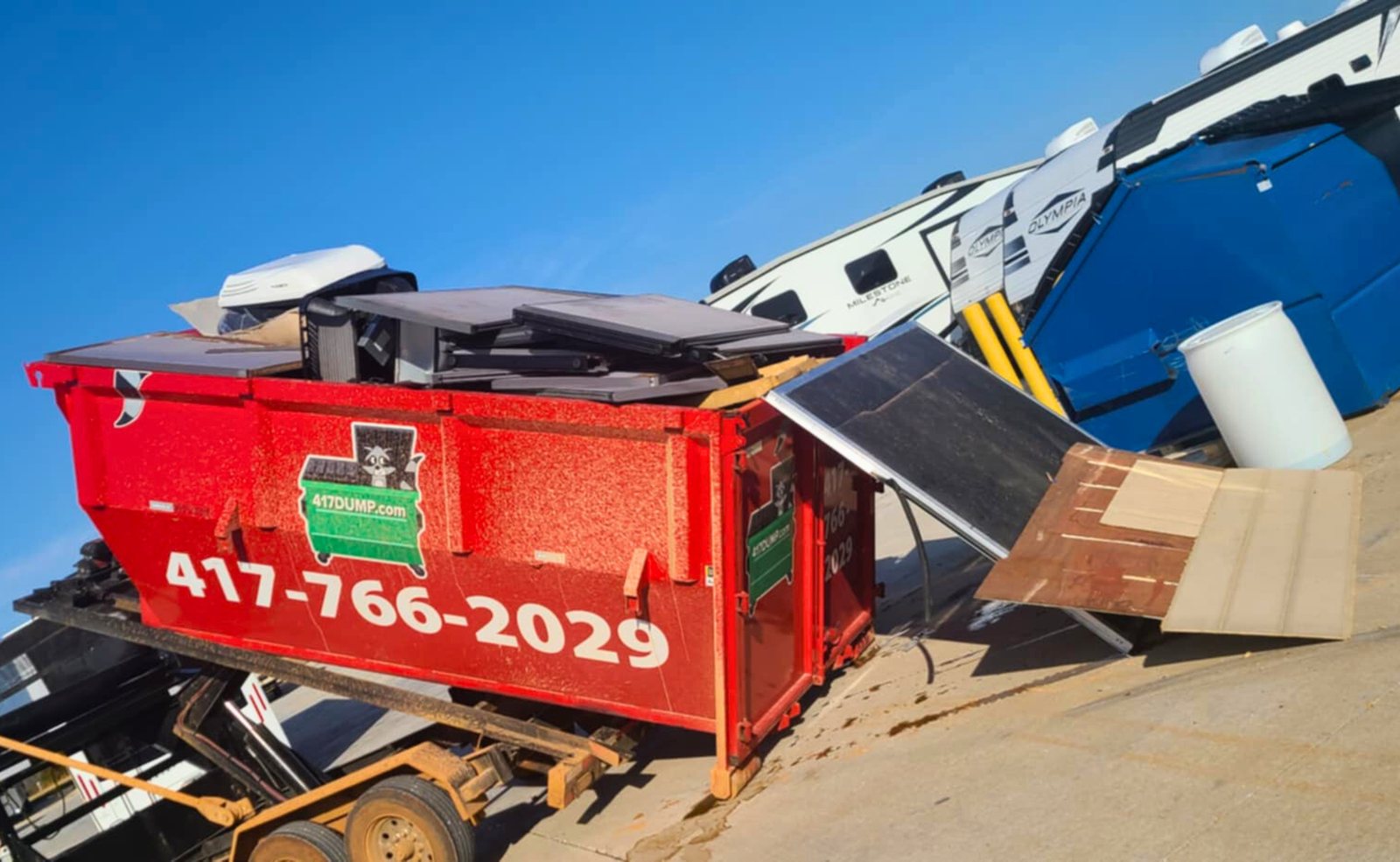 Red roll-off dumpster on a trailer loaded with demolition debris.