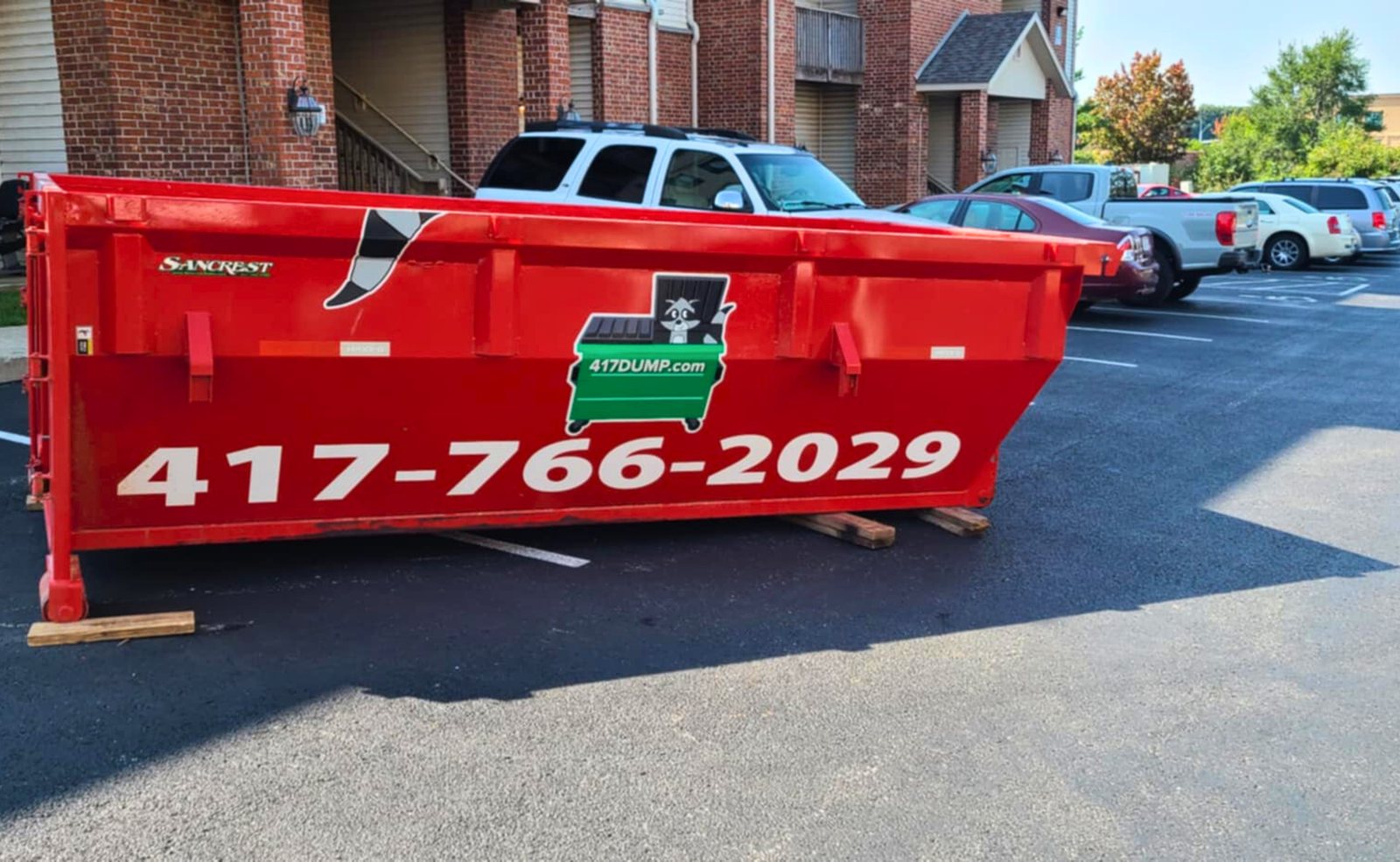 Red roll-off dumpster in the parking lot of an apartment complex