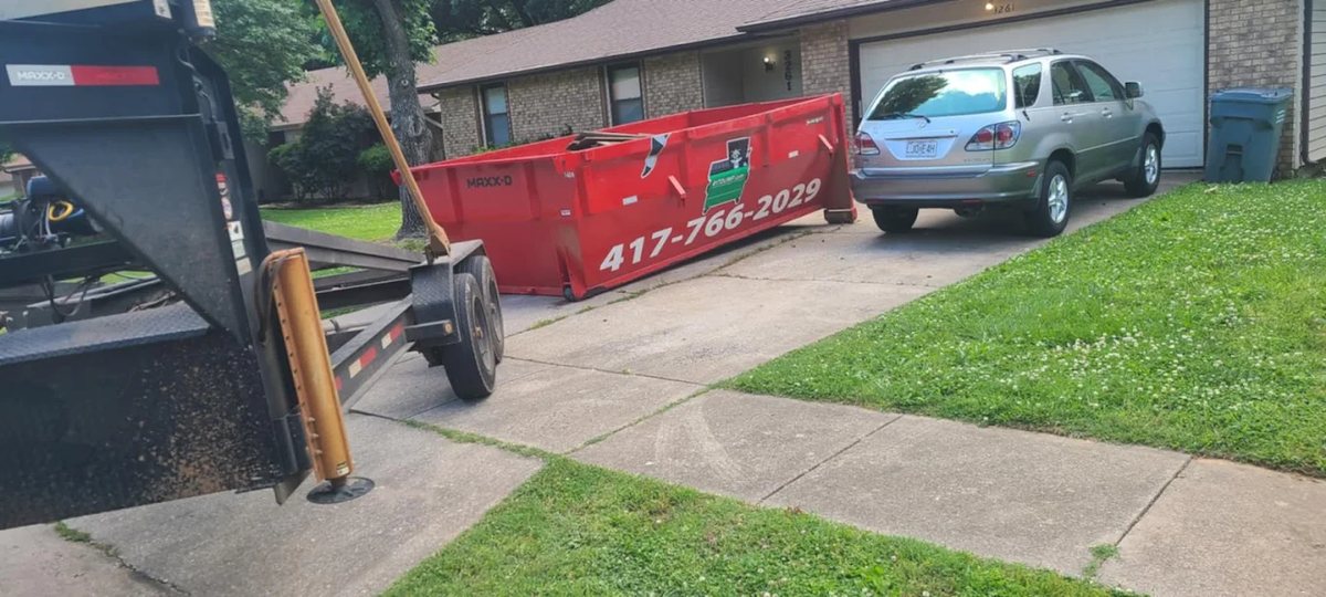 Red roll-off dumpster on a residential driveway beside a parked car