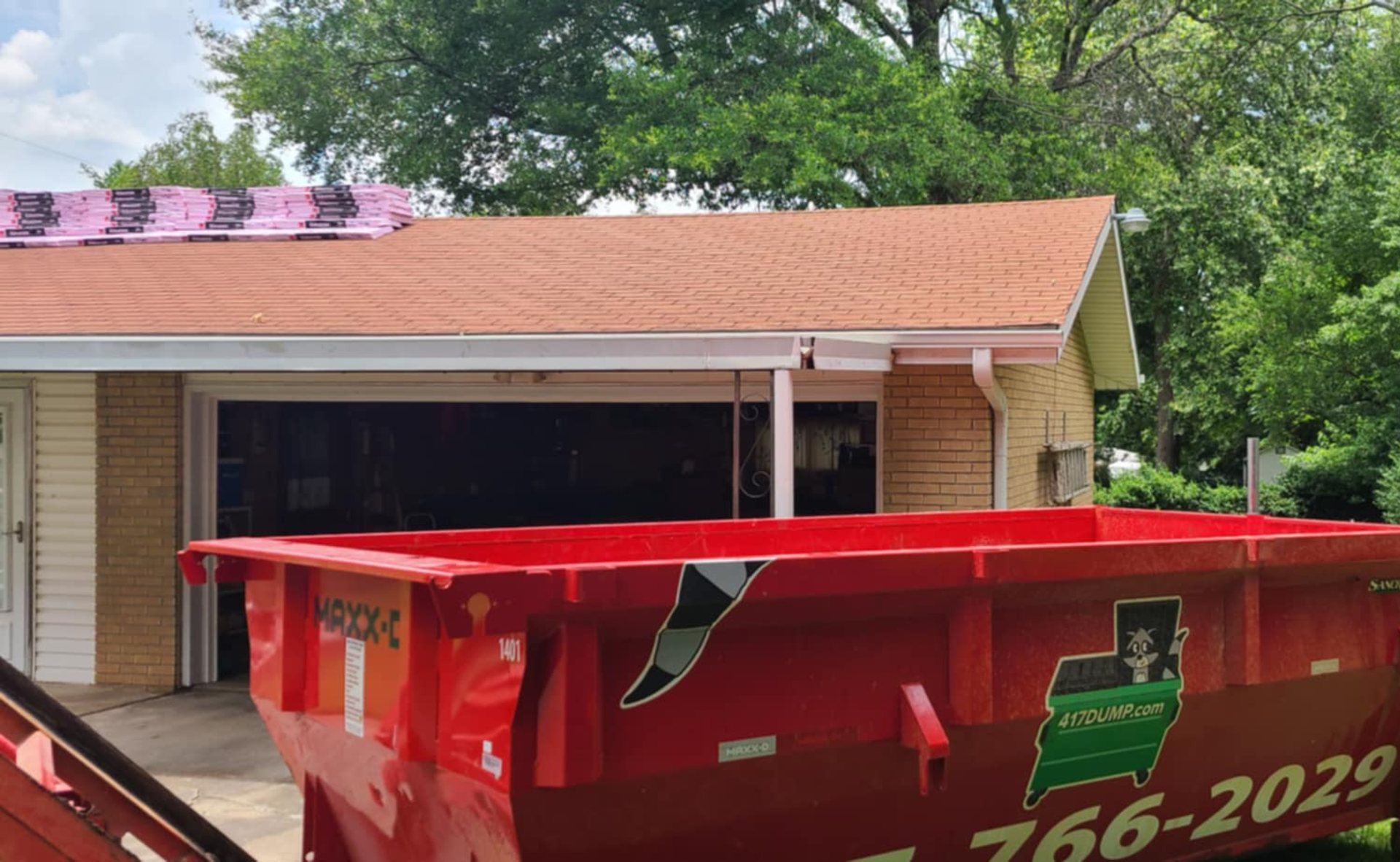 A red 417 Dumpster Rental roll-off dumpster in front of a house with a covered porch.