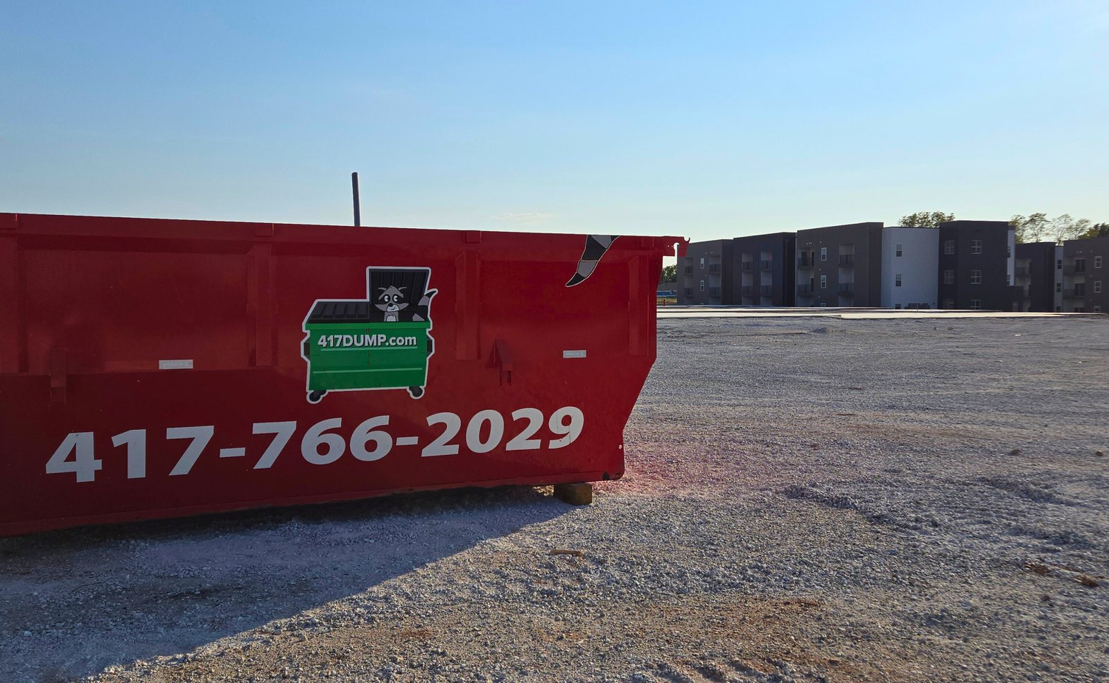 Red 417 Dumpster Rental roll-off sitting on a gravel lot with apartment buildings in the background.