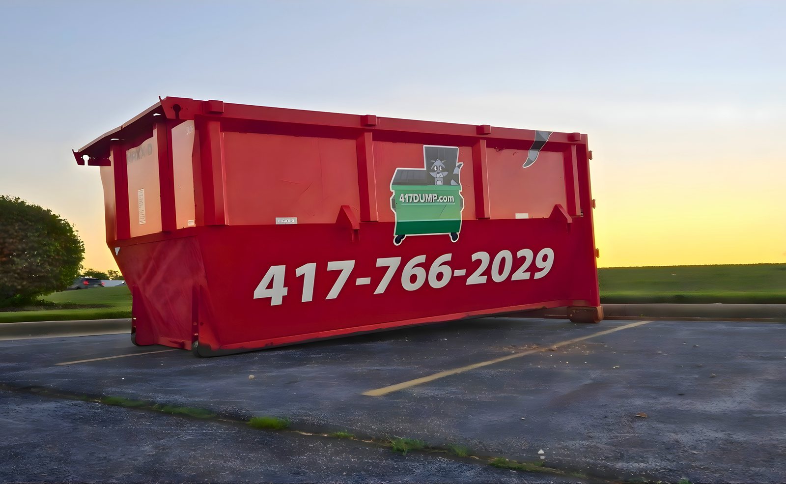 Red roll-off dumpster in a parking lot at sunset