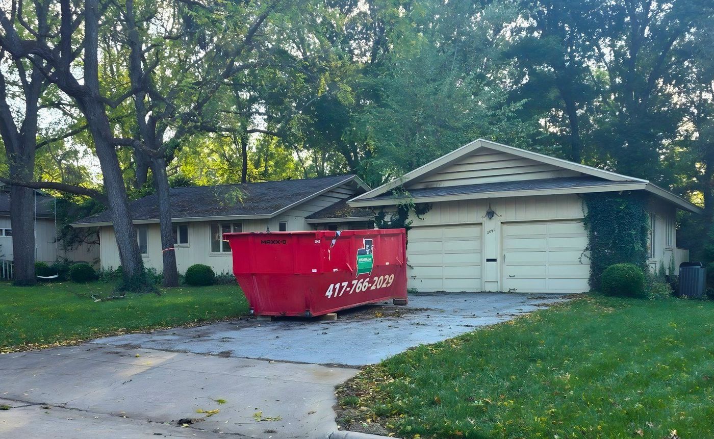 A 417 Dumpster Rental trailer setting a roll-off down gently on a residential driveway in Springfield, MO
