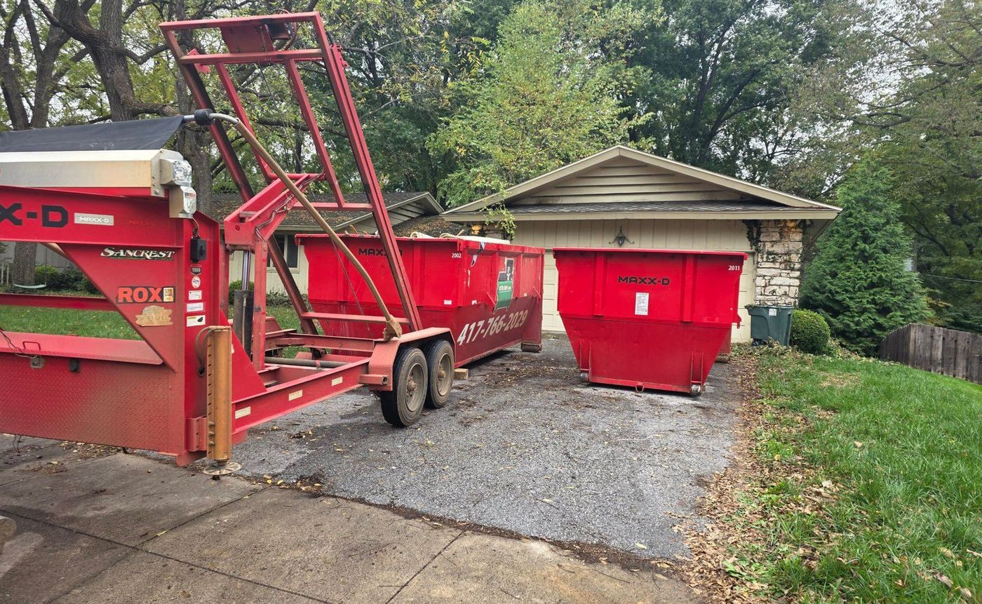 Hydraulic lift tilting a red roll-off dumpster onto a residential driveway