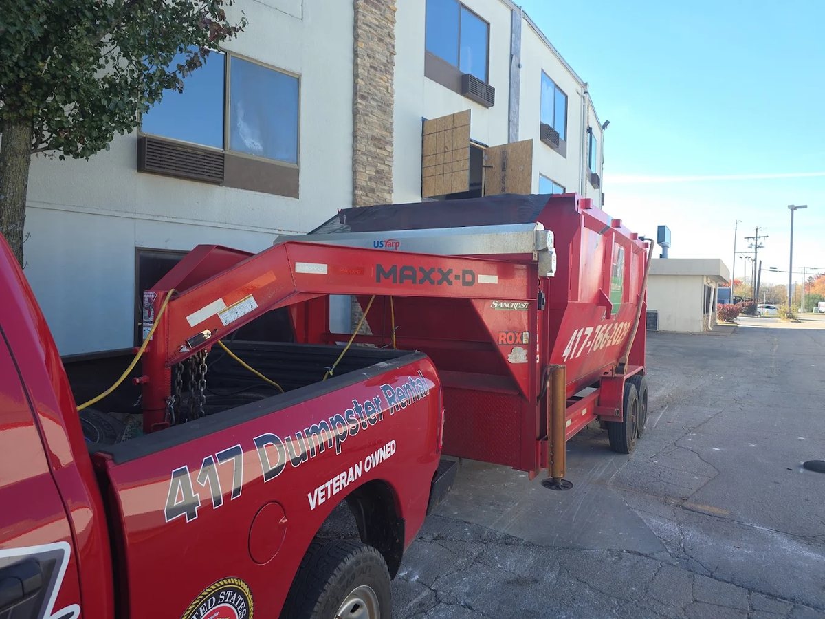 417 Dumpster Rental truck and trailer delivering a dumpster at a commercial building