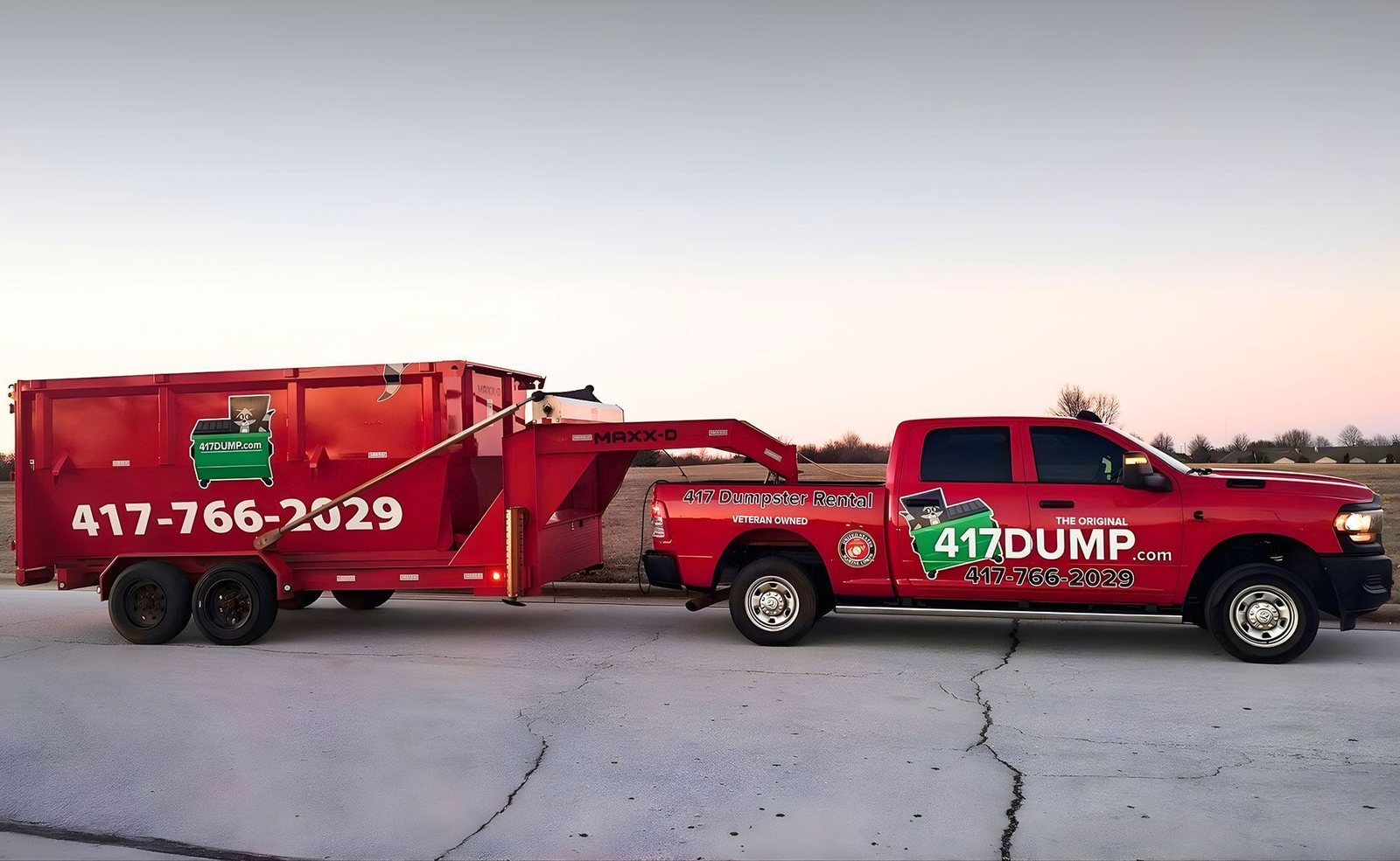 417 Dumpster Rental pickup and trailer hauling a red dumpster at dusk